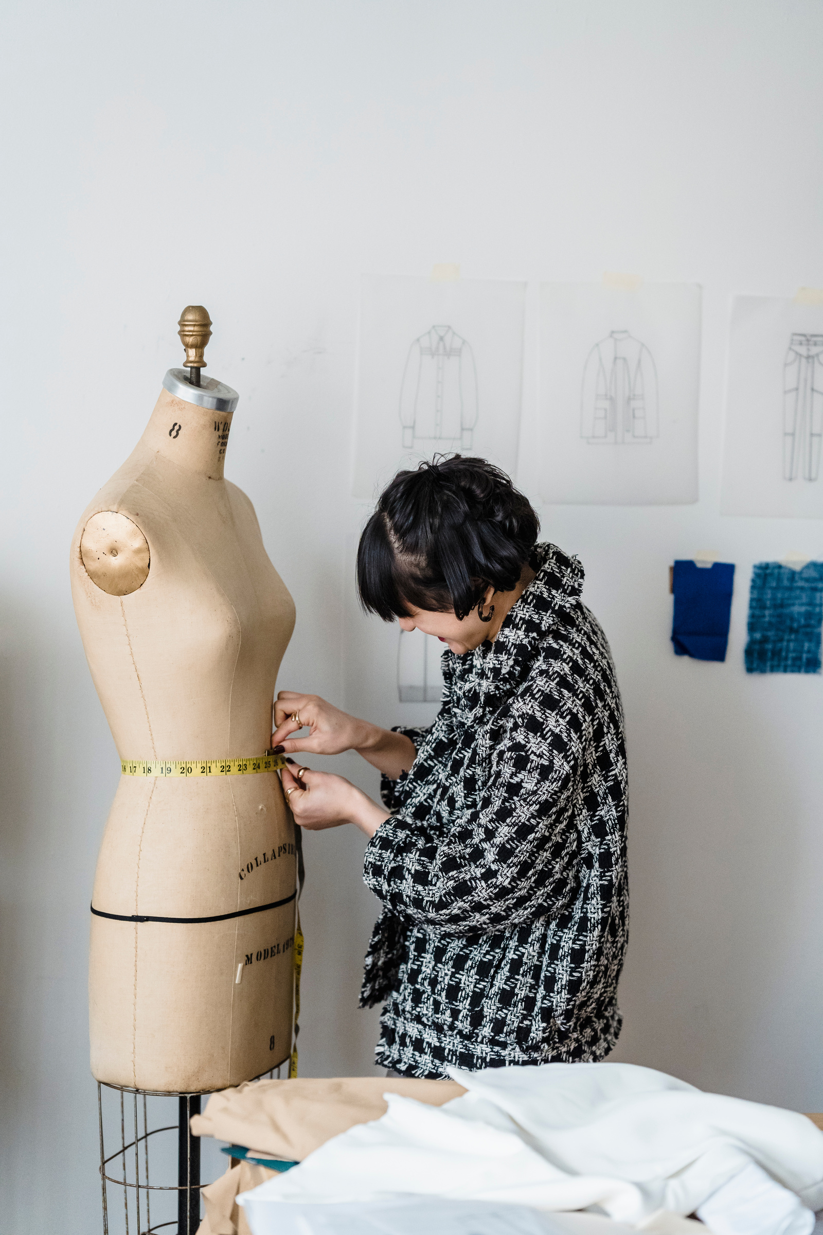 Seamstress measuring waist of mannequin with tape in workshop